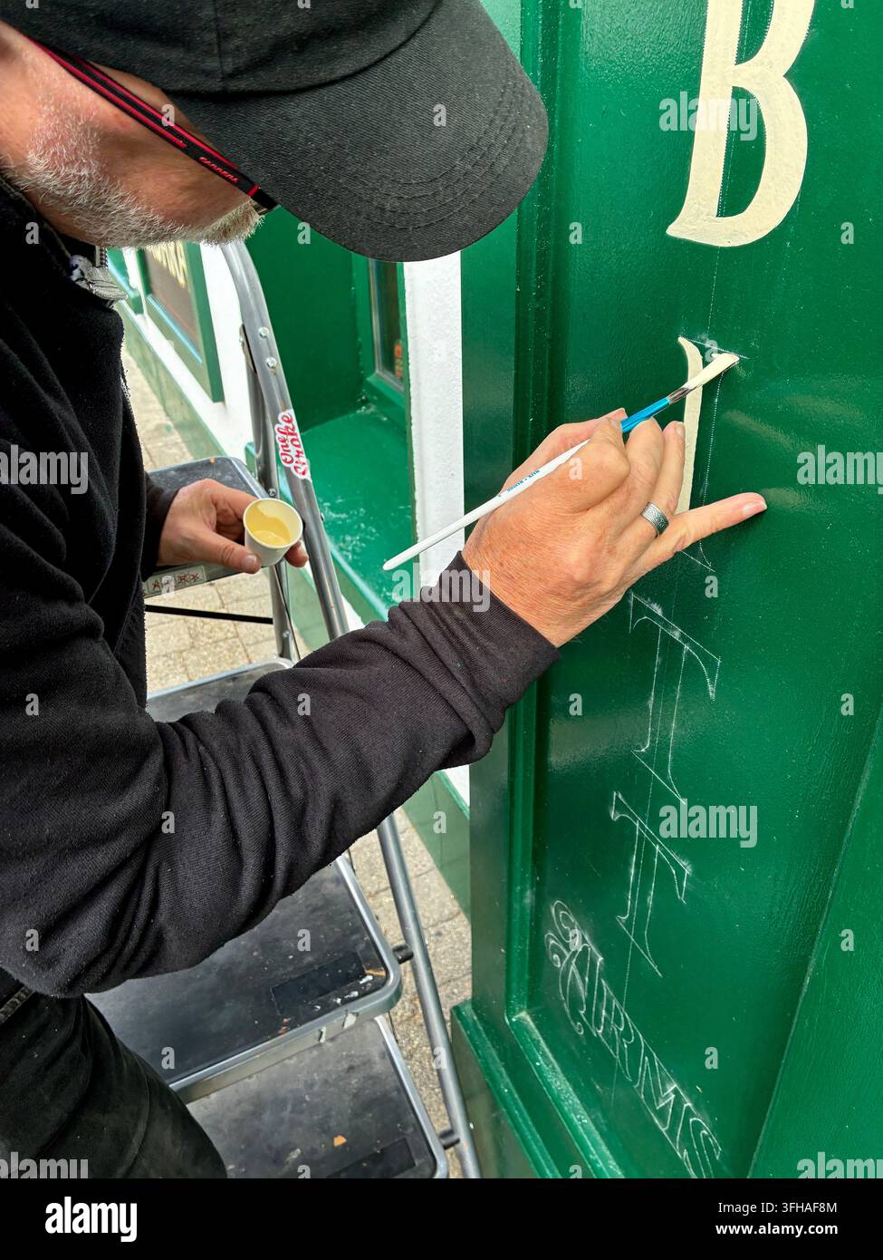 Schildermaler bei der Arbeit an der Hotelfassade. - Smartphone-aufgenommenes Stockfoto