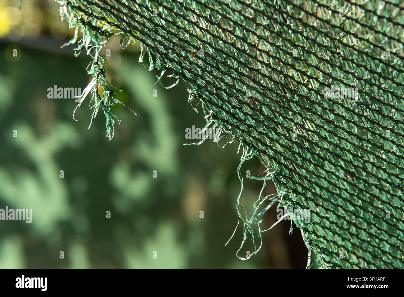 Beschädigtes grünes Plastik-Sonnenseitennetz mit zerrissenem Rand und Kopierraum Stockfoto