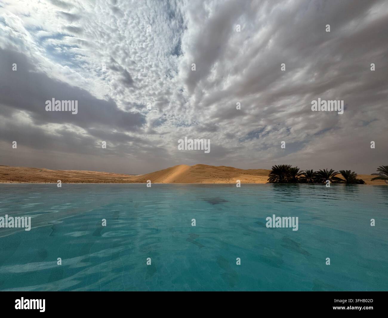 Resort-Pool mit Blick auf Wüstendünen unter dramatischen Wolken in Abu Dhabi, Vereinigte Arabische Emirate - Smartphone-aufgenommenes Stockfoto