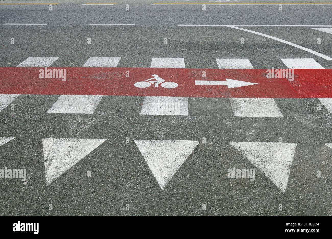 Rotes Fahrradweg-Schild entlang eines Zebrastreifens, mit einem gemalten Vorfahrtszeichen vorne. Urbane Straße im Hintergrund. Stockfoto
