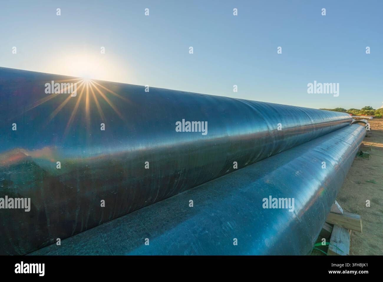 Ansicht von großen beschichteten Stahlrohren, die für den Bau einer Erdgas-Pipeline entlang der Piombino-Livorno-Linie gestapelt sind, mit Sonnenstern-Brennfleck. Livorno, Toskana, Italien Stockfoto