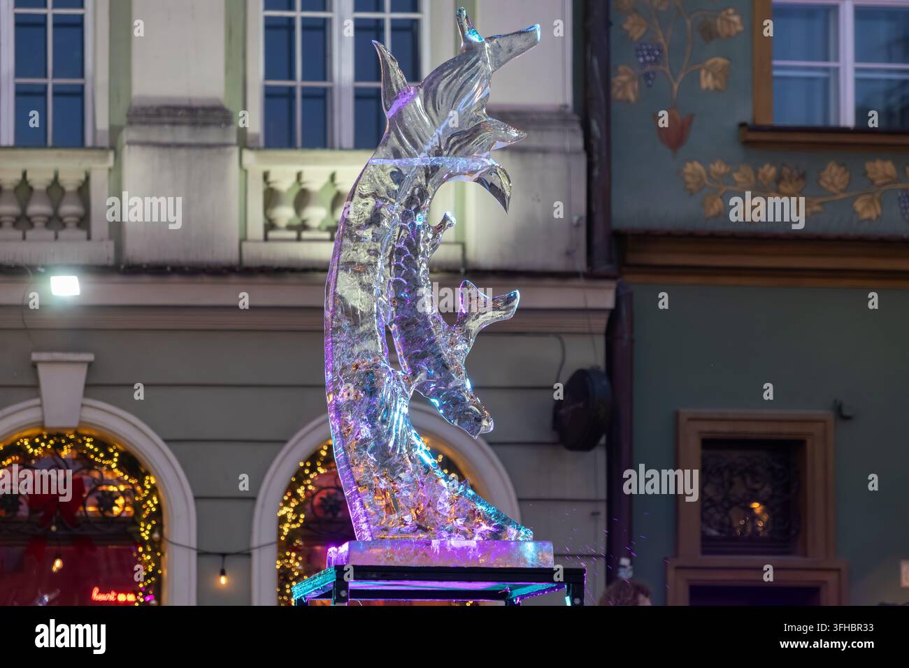 Nahaufnahme einer schimmernden Eisskulptur, beleuchtet von farbenfrohen lila und blauen Lichtern, die einen bezaubernden künstlerischen Blickfang in einer nächtlichen Stadt schaffen Stockfoto
