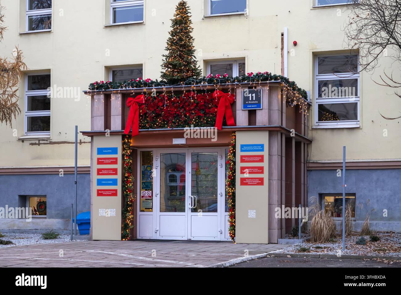 Posen, Polen - 13. Dezember 2025: Weihnachtsdekorationen schmücken den Eingang des Gebäudes mit leuchtenden Kiefernbaumlichtern und roten Bändern, um eine festliche Stockfoto