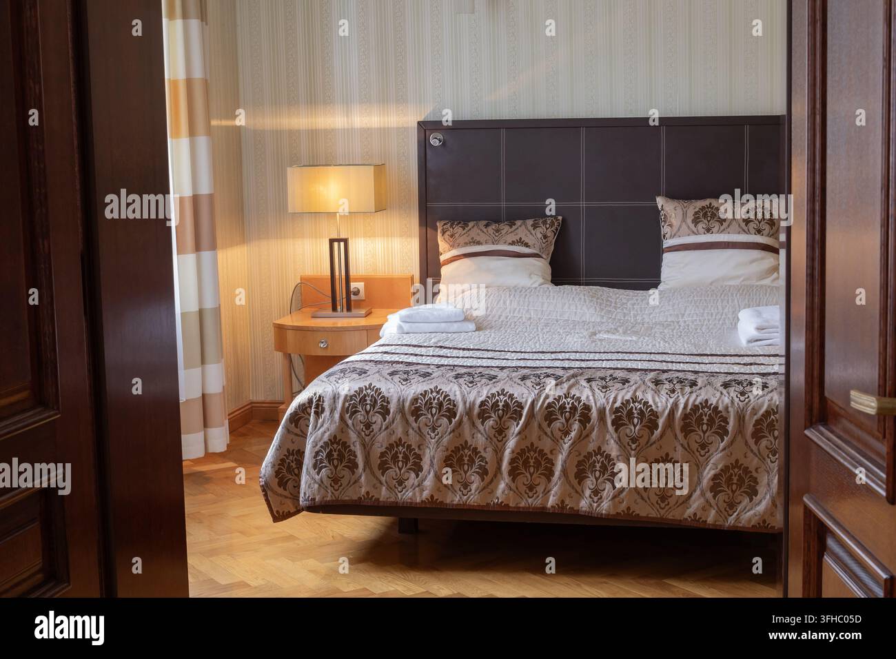 Ein ordentlich eingerichtetes Schlafzimmer mit einem Doppelbett, Nachttischlampen und gefalteten Handtüchern, inszeniert für eine Apartmentvermietung oder eine Immobilienmaker-Listung. Stockfoto