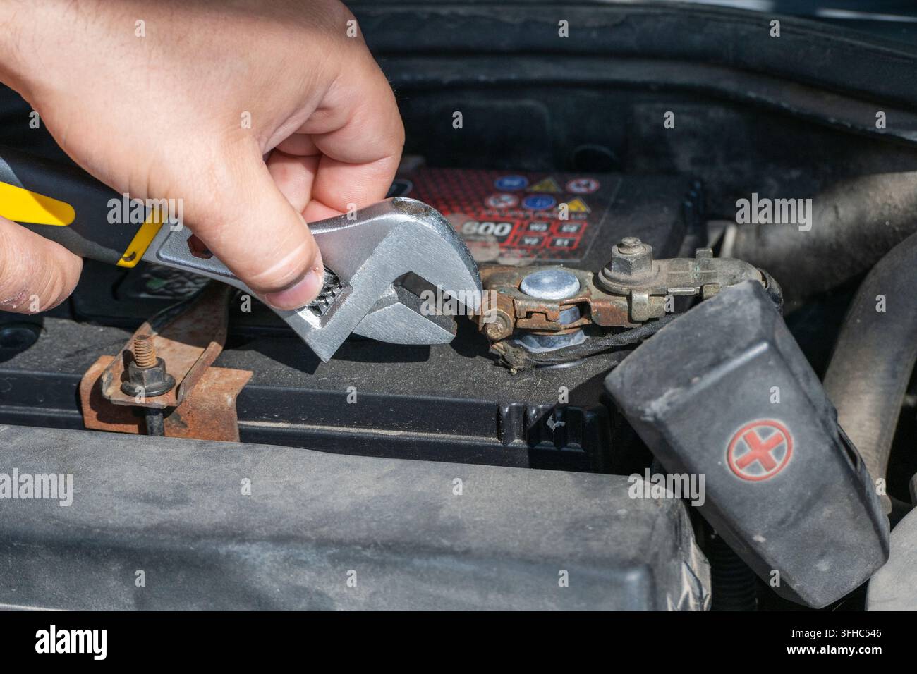 Die Hände einer Person verwenden einen verstellbaren Schraubenschlüssel, um die Mutter an der positiven Klemmleiste einer Autobatterie unter der Haube zu lösen oder anzuziehen. Stockfoto