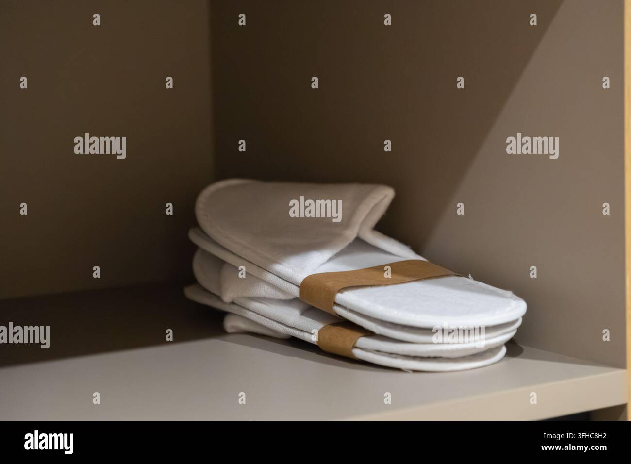 Weiße Stoffpantoffeln für Gäste sind ordentlich in einem Holzschrank gestapelt und bieten eine unverzichtbare Annehmlichkeit, die für eine entspannende und bequeme Ex... Stockfoto