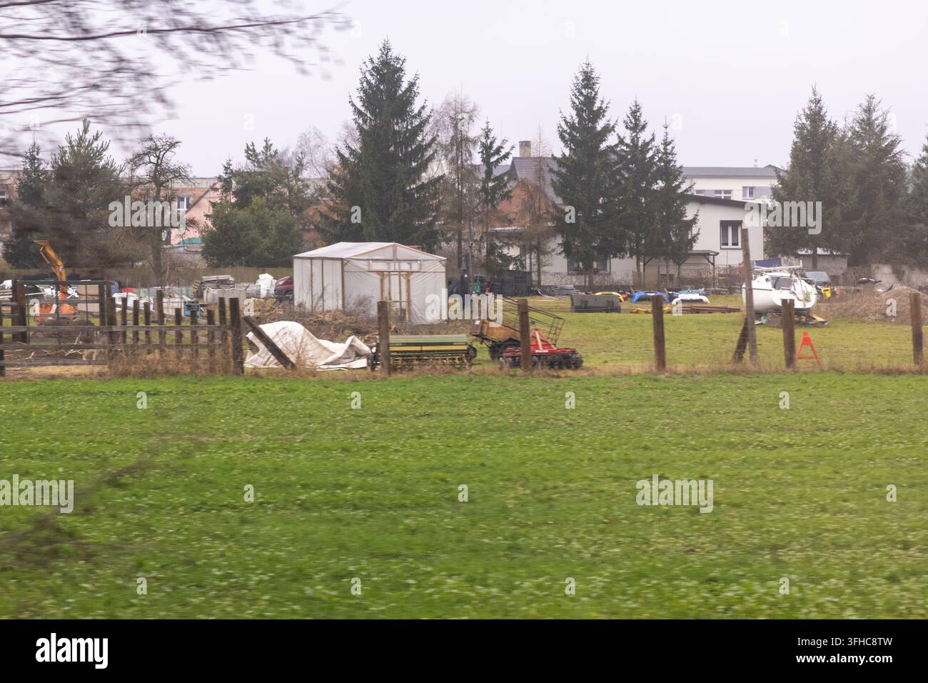 Der Außenhofbereich zeigt Landwirtschaftswerkzeuge, ein Gewächshaus und verschiedene Geräte, die auf einem grasbewachsenen Grundstück gelagert sind, und veranschaulicht typisches Grundstücksmanagement wit Stockfoto