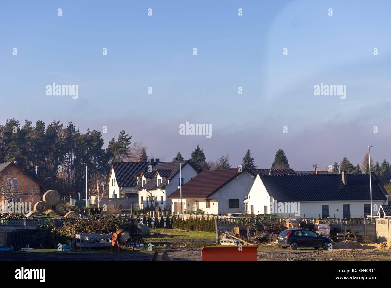 Leszno, Polen – 15. Dezember 2025: Vorstadthäuser, die sich an einen dichten Wald in einer ländlichen Umgebung schmiegen, wo landwirtschaftliche Ballen und klarer Himmel ca Stockfoto