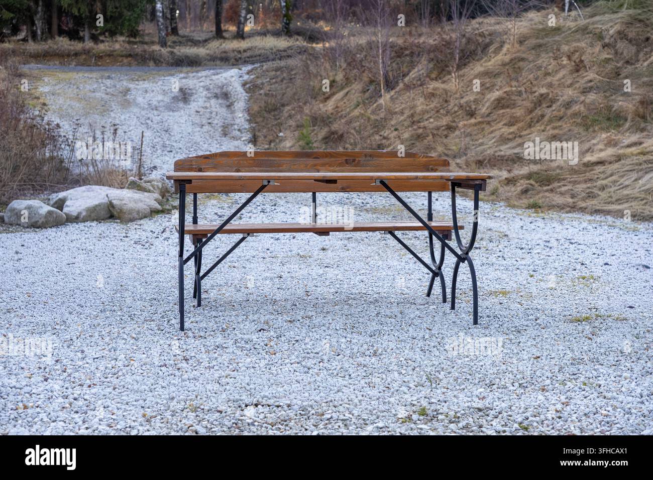 Ein leerer Holz-Picknicktisch mit einem robusten schwarzen Metallrahmen steht auf einem frostigen Kiesboden und deutet auf einen ruhigen Außenbereich zum Essen hin, umgeben von Stockfoto