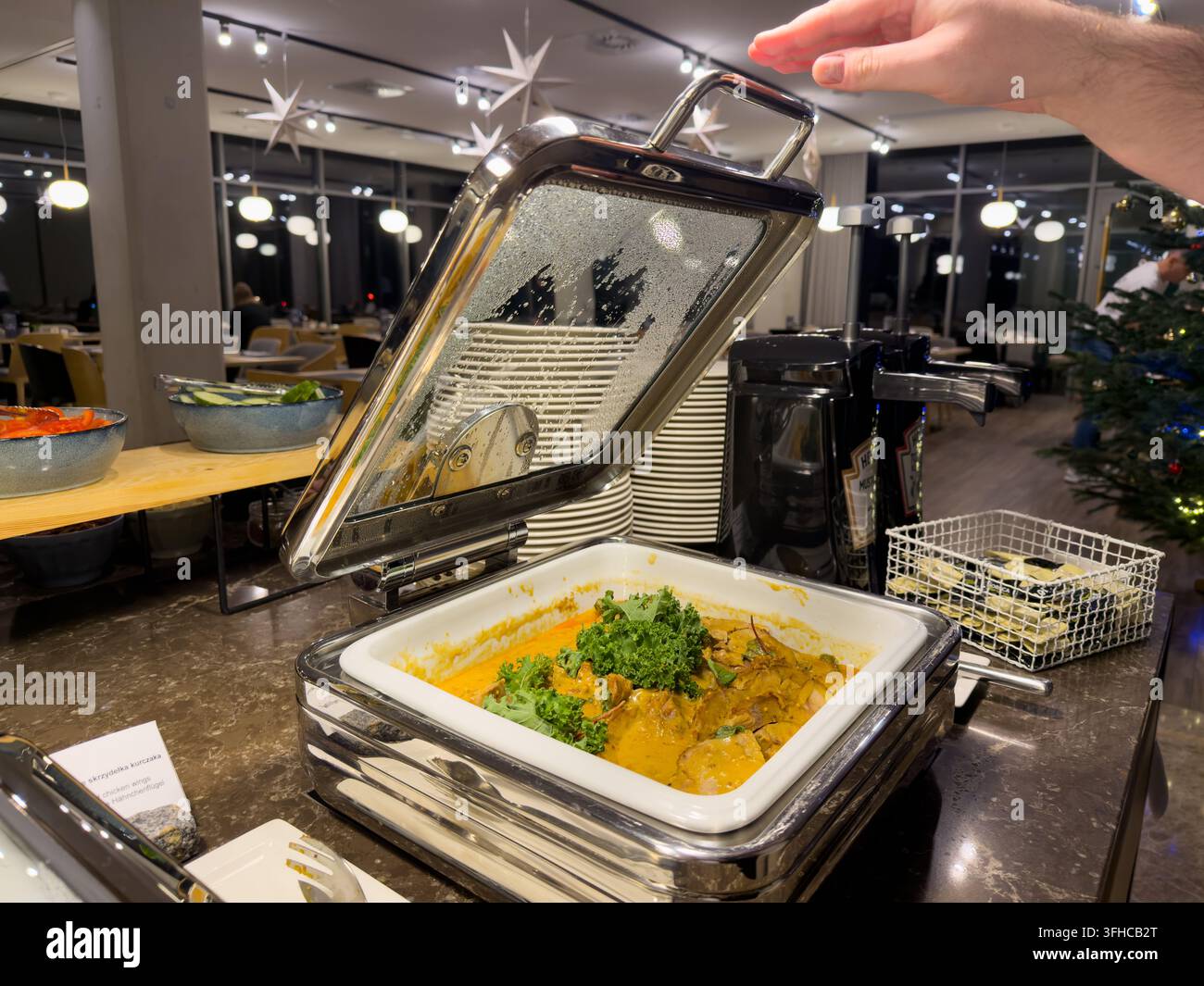 Nahaufnahme einer Hand, die heiße Hähnchenflügel aus einem Speisenwärmer an einem modernen Hotelbuffet serviert, das während abendlicher Veranstaltungen Selbstbedienung anbietet Stockfoto
