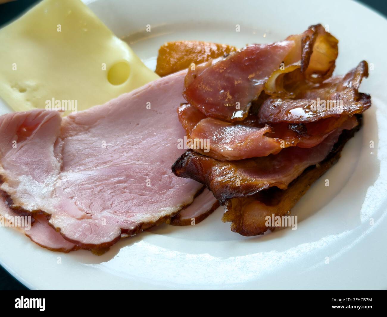 Nahaufnahme eines köstlichen Frühstücks mit herzhaften Schinkenscheiben, goldbraunem knusprigem Speck und Schweizer Käse, perfekt für ein Hotel-Buffet-Frühstück Stockfoto
