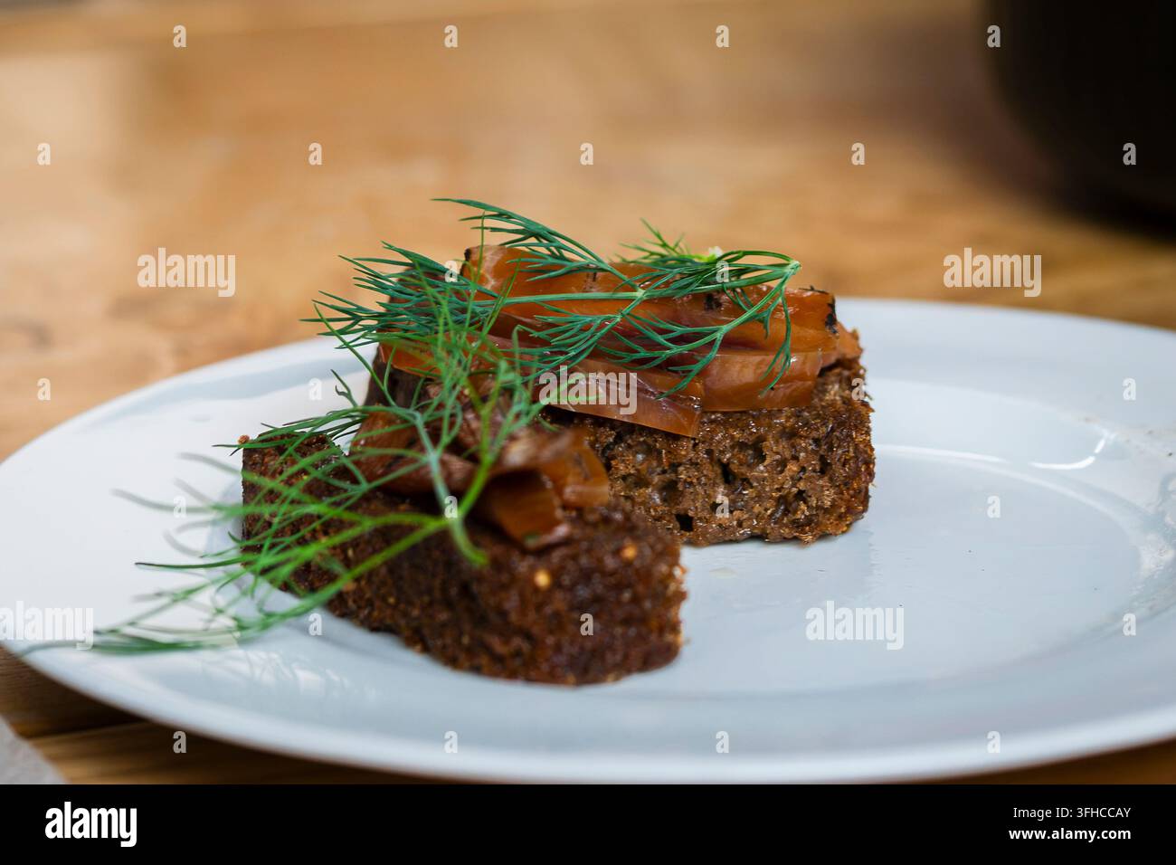 Gekochter Schleienfisch auf traditionellem dunklem Roggenbrot, belegt mit zarten Orangenfischstücken und frischem Dill, serviert auf einem weißen Teller. Stockfoto
