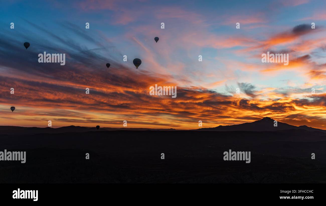 Heißluftballons in der Morgendämmerung über Kappadokien, mit dem Berg Erciyes, der sich unter orangefarbenen und rosa Wolken abzeichnet, Türkei. Stockfoto