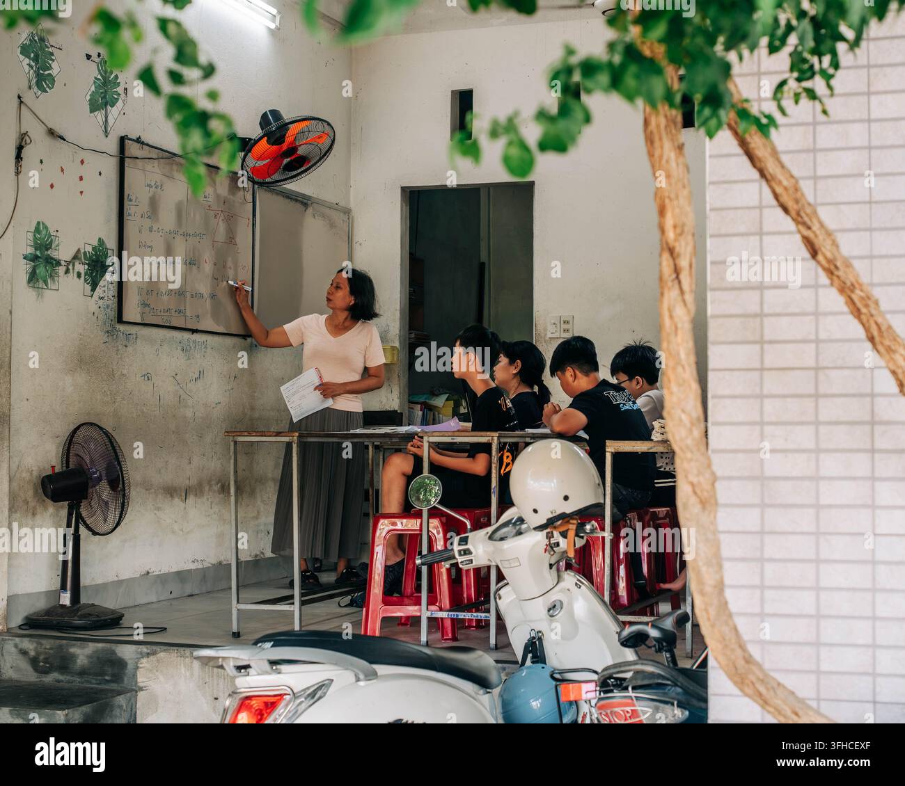 Hue, Vietnam – 9. September 2026. Eine Lehrerin schreibt an einer Tafel, während Schulkinder an Pulten sitzen und einem Unterricht in einem bescheidenen Klassenzimmer folgen. Stockfoto