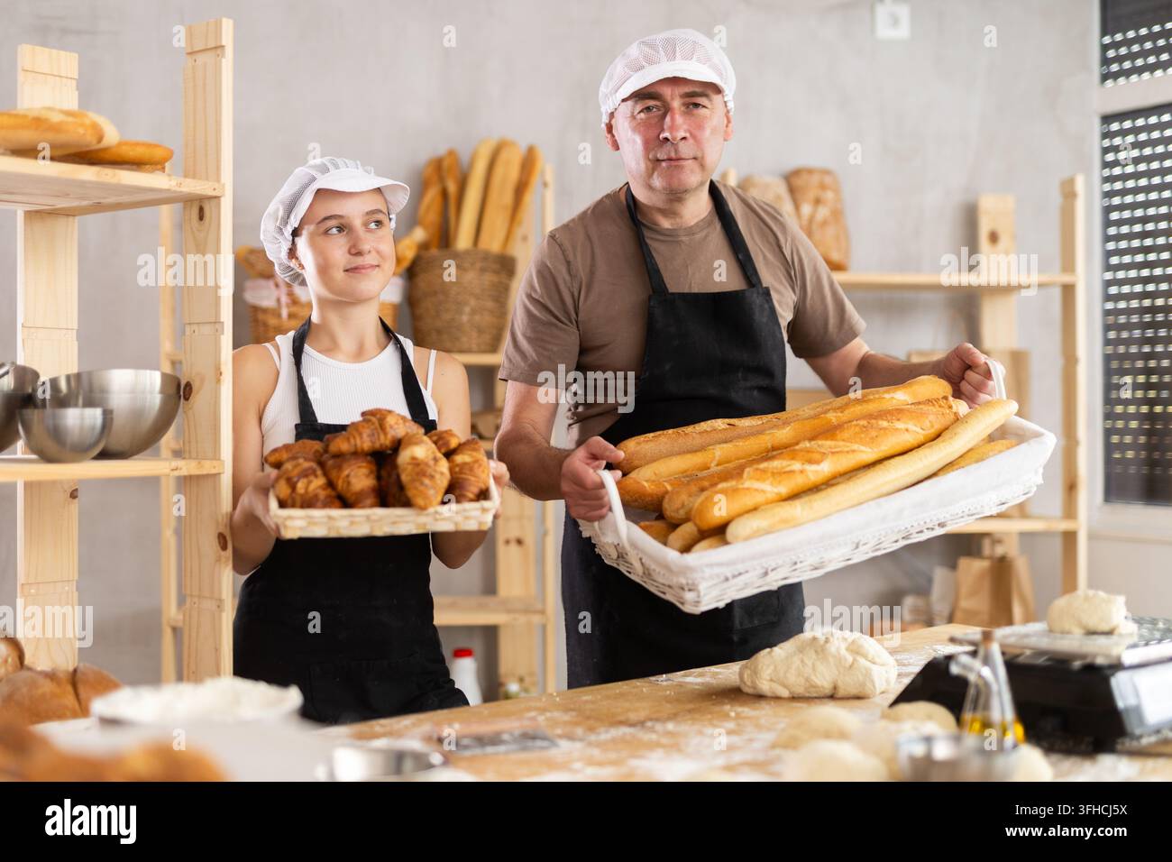 Heimische Brotproduktion, Arbeitsraum. Opa und Teenager-Schülerin stehen in der Küche mit einem Korb voller fertiger Produkte wie Baguettes und Croissants. Mädchenanteil Stockfoto