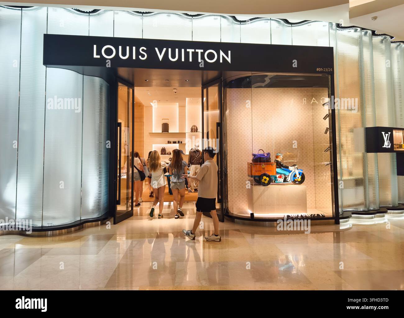 Louis Vuitton-Fassade, die eine beleuchtete Glasfront und eine Schaufensterauslage mit einem dekorativen Motorrad zeigt. Ion-Einkaufszentrum, Singapur Stockfoto