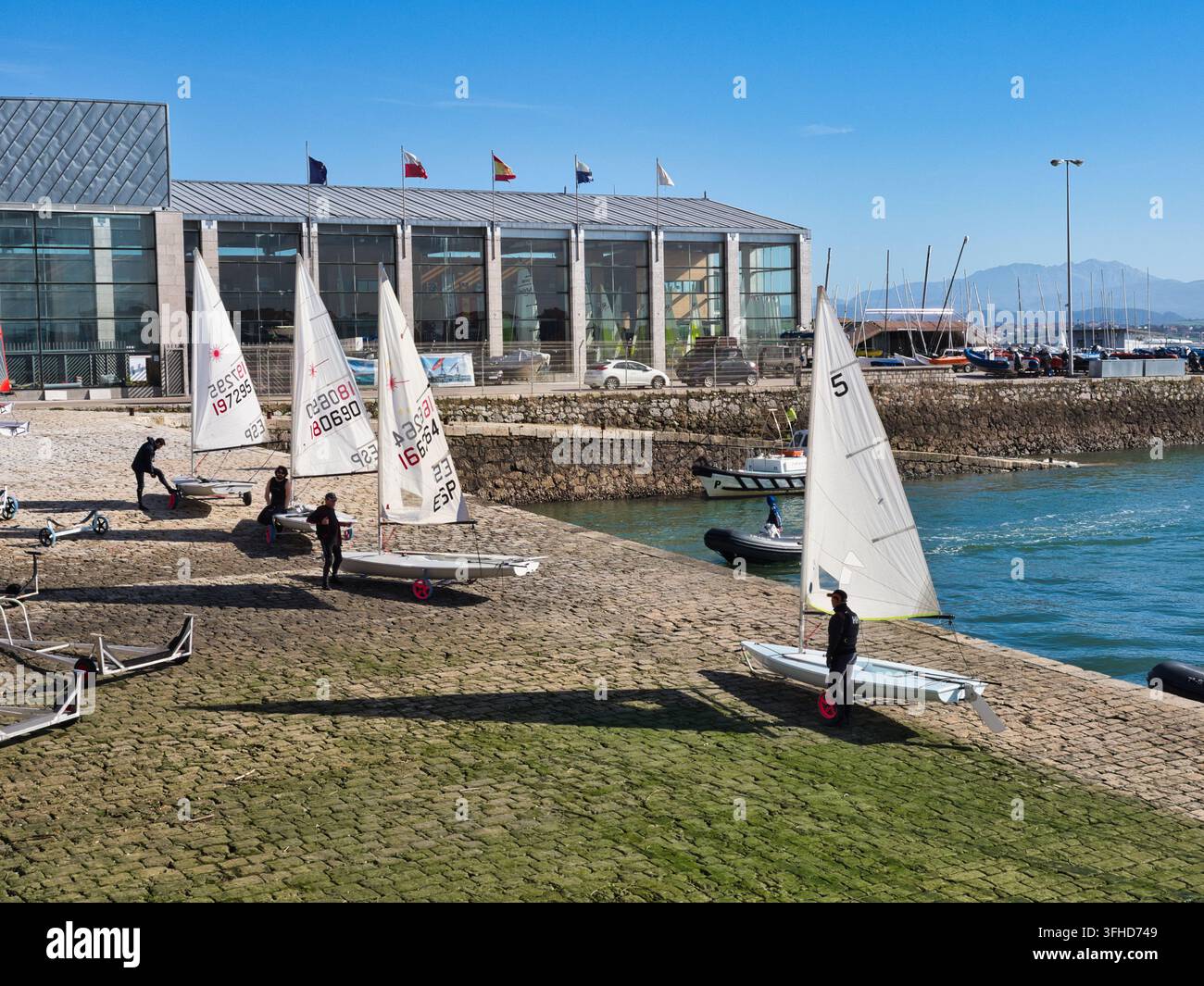 Segelschule an der Marina - Junge Segler bereiten kleine Segelboote für eine Trainingseinheit an einem sonnigen Tag bei einem modernen Yachtclub an einer malerischen Küste vor Stockfoto