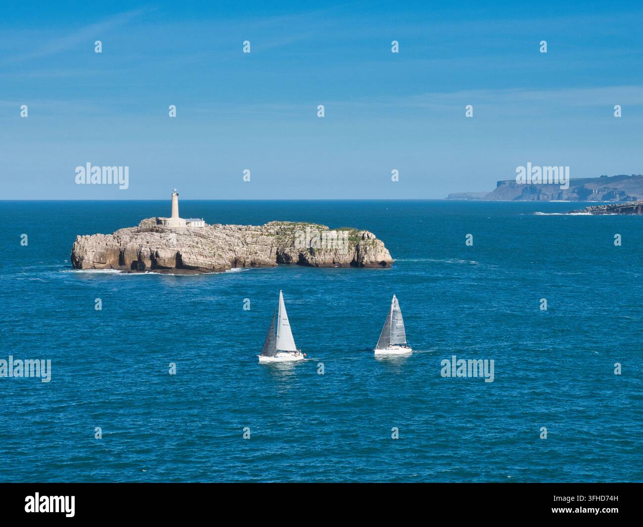 Leuchtturm auf Rock Island mit Yachten - Panoramablick auf Segelboote, die in den offenen blauen Meeresgewässern in der Nähe einer Küsteninsel navigieren, die einen historischen Strand bietet Stockfoto