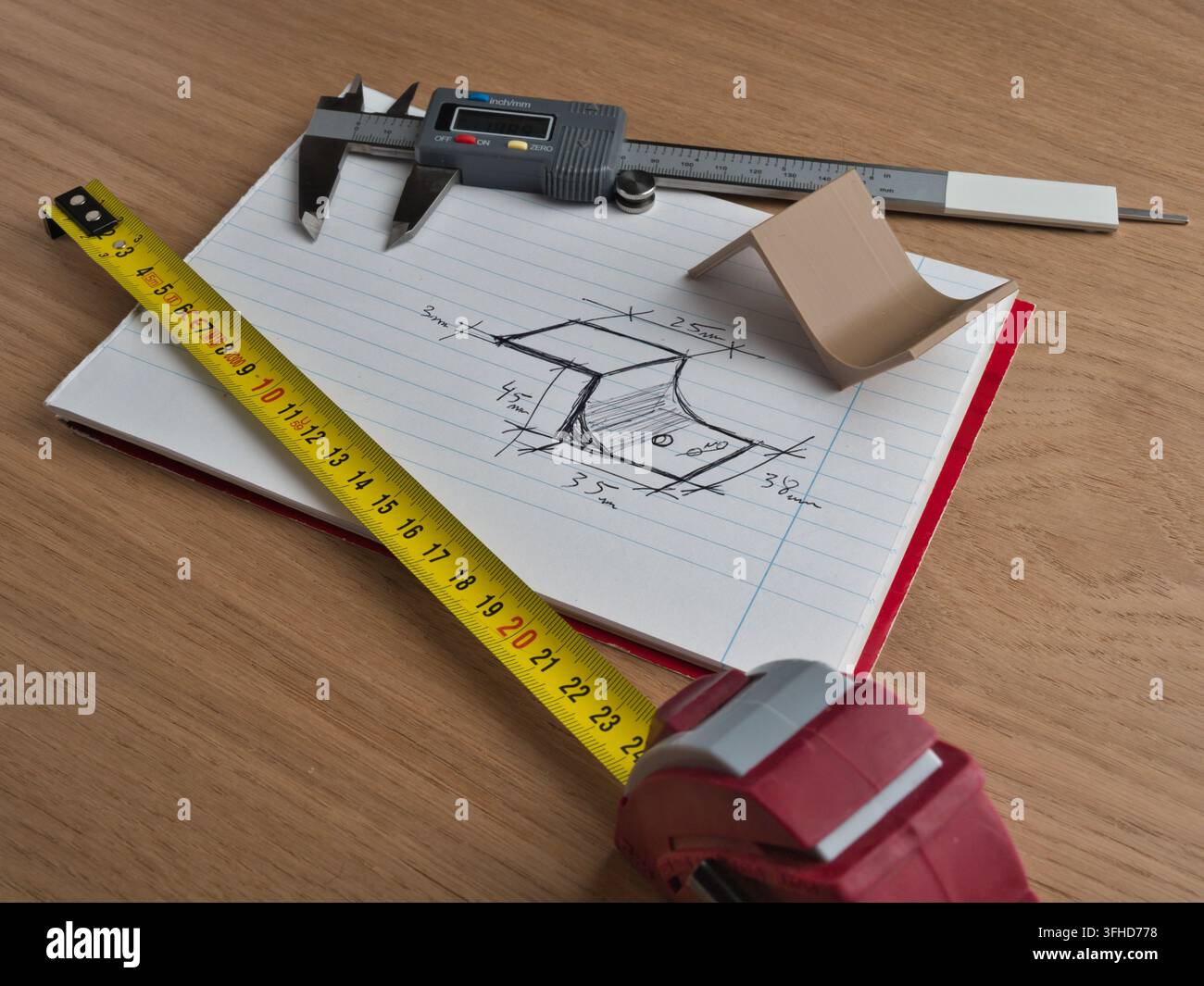 Technisches Design und Messwerkzeuge - Digitales Messschieber und Maßband über einer technischen Skizze eines mechanischen Teils auf einem Notizblock auf einem Holzwo Stockfoto