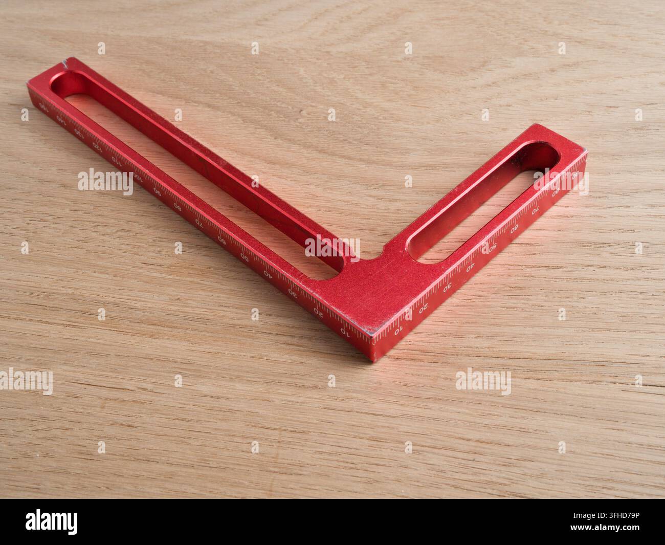 Roter Aluminium-Schreinerwinkel auf Holz – Ein eloxierter roter Aluminium-L-Winkel mit Millimetermaßstabmarkierungen, der auf einer hellen Holzoberfläche ruht. Stockfoto