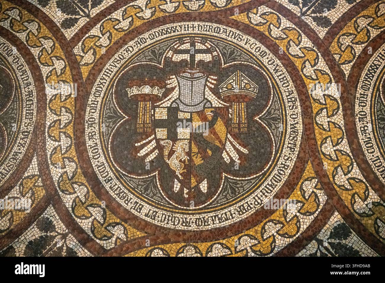 Nahaufnahme eines heraldischen Mosaiks mit einem Adleremblem und lateinischer Inschrift auf dem Boden des Kölner Doms. Stockfoto