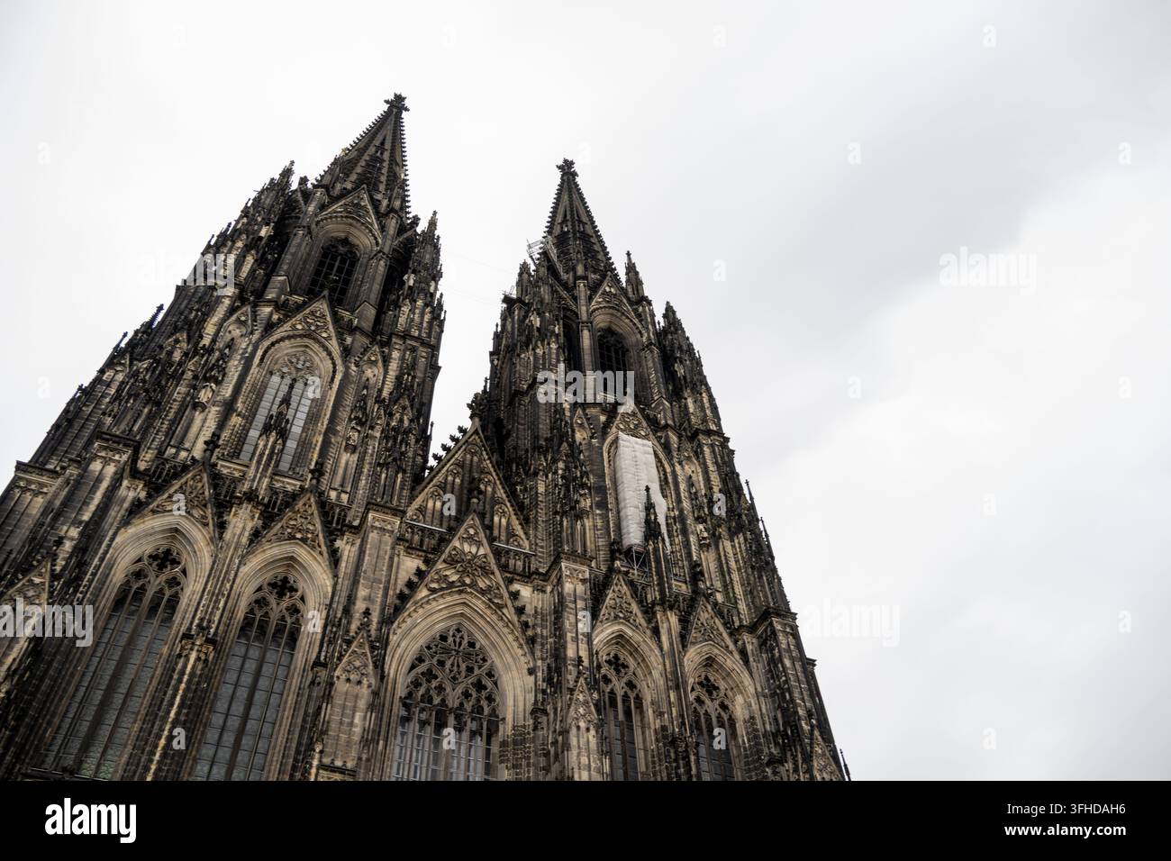 Niedrigwinklige Ansicht der Zwillingsspitzen und der kunstvoll verzierten gotischen Fassade des Kölner Doms unter einem bewölkten Himmel in Köln, Deutschland. Stockfoto