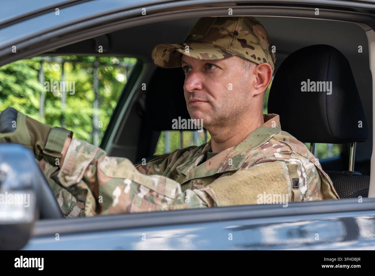 Ein Soldat in Tarnuniform fährt ein Auto, während er nach vorne schaut. Stockfoto
