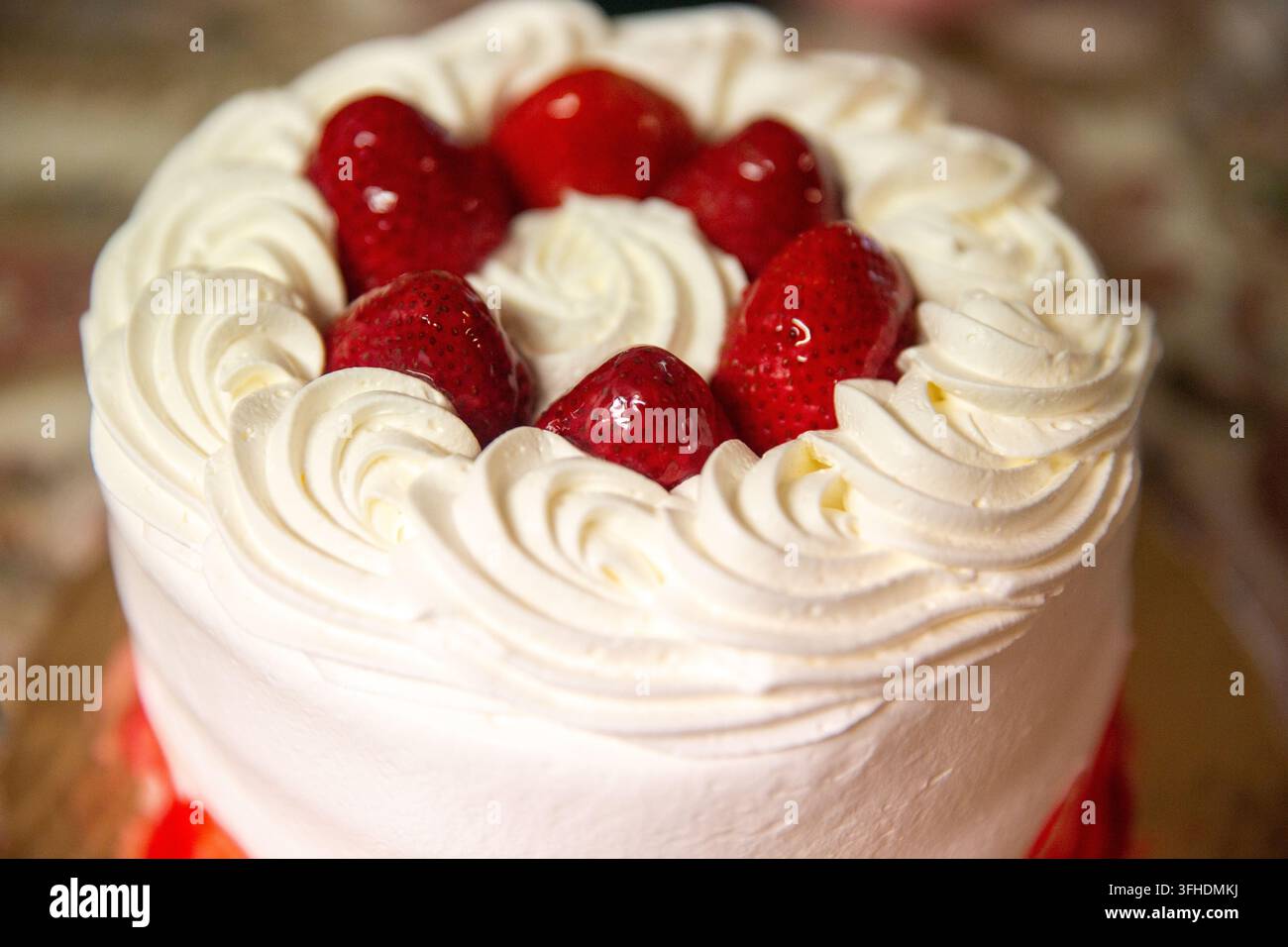 Ein detailliertes Lebensmittelbild, das einen runden weißen Sahnekuchen zeigt, der mit frischen, glänzenden roten Erdbeeren und gezogenen Zuckerguss-Spiralen dekoriert ist. Stockfoto
