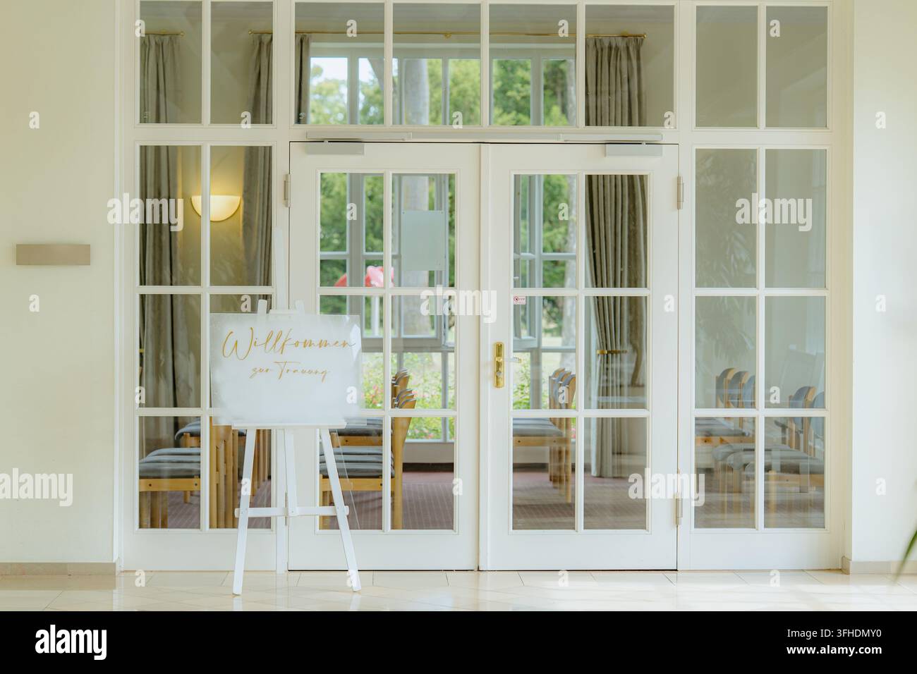 eleganter Innenbereich für eine Hochzeitsfeier mit Glastüren und Holzstühlen, der Gäste zu einer formellen Zeremonie einlädt, Vorderansicht Stockfoto