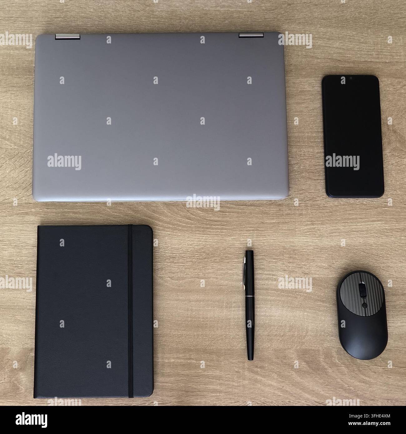 Minimalistische Topansicht eines aufgeräumten Büroschreibtisches mit einem geschlossenen grauen Laptop, schwarzem Notizbuch mit Gummiband, eleganter Stift, moderner kabelloser Maus und Smartph Stockfoto