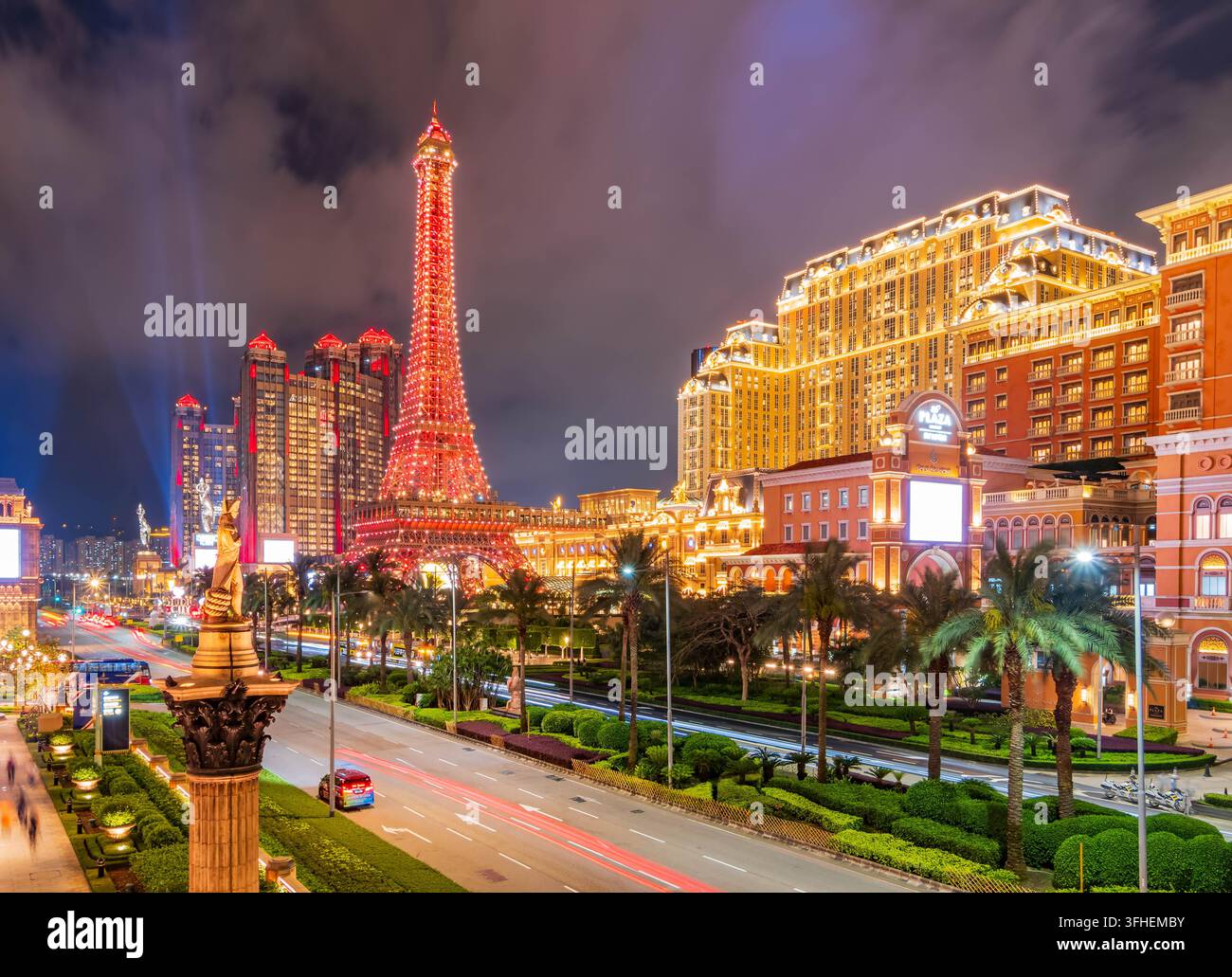 Macau, China, 16. APR 2024 – Die Nachbildung des Eiffelturms steht in rotem Licht beleuchtet neben großen Hotels mit goldenen Fassaden, während der Verkehr fließt Stockfoto