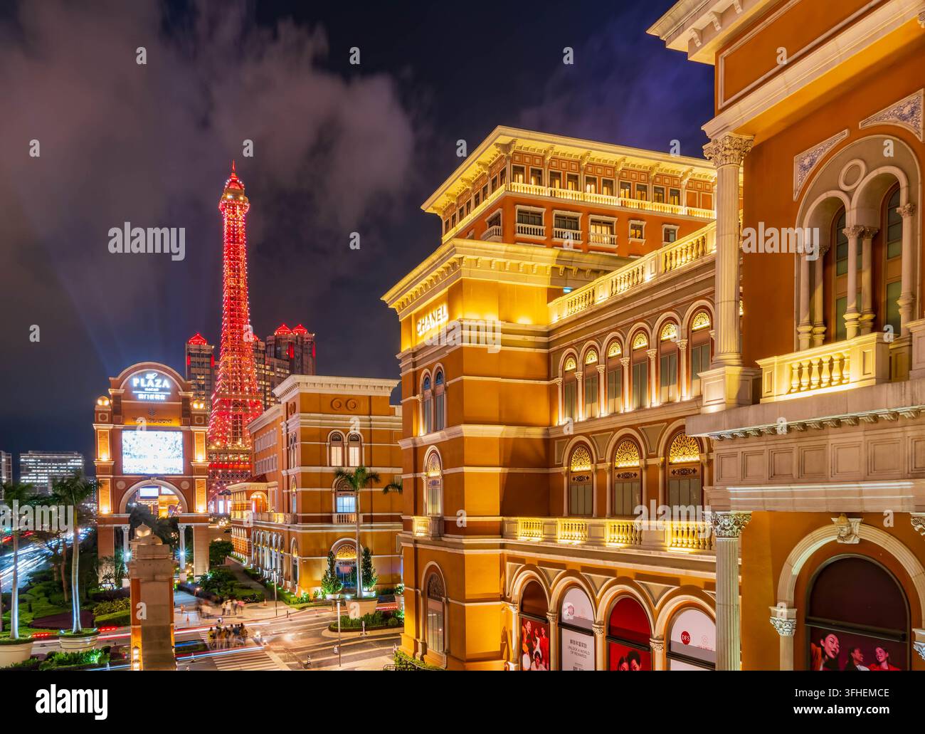 Macau, China, 16. APR 2024 – Ein leuchtend roter Turm erhebt sich im Hintergrund, während großartige Gebäude im europäischen Stil mit warmer Beleuchtung eine Stockfoto