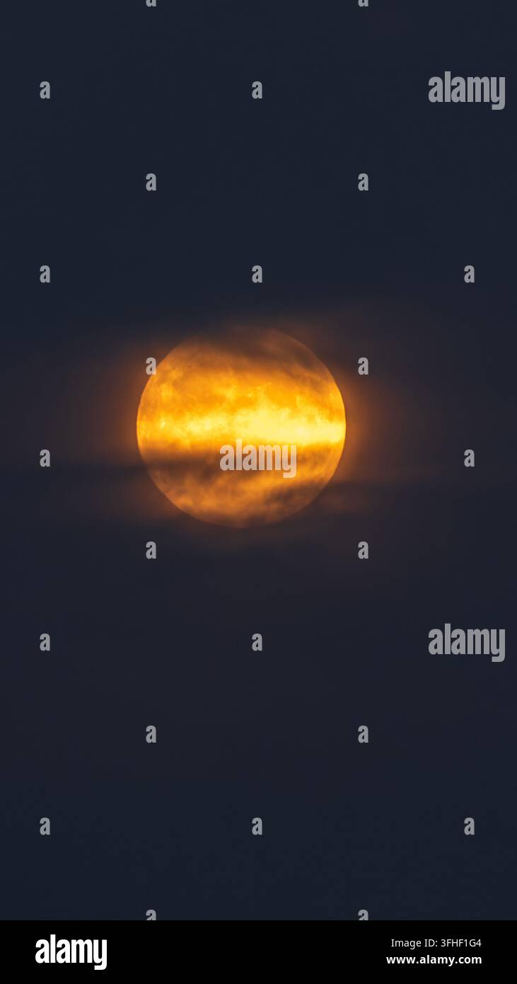 Oranger Vollmond, der nachts durch Wolken scheint, atmosphärische natürliche Landschaft, kommerzielles Stockmaterial Stockfoto