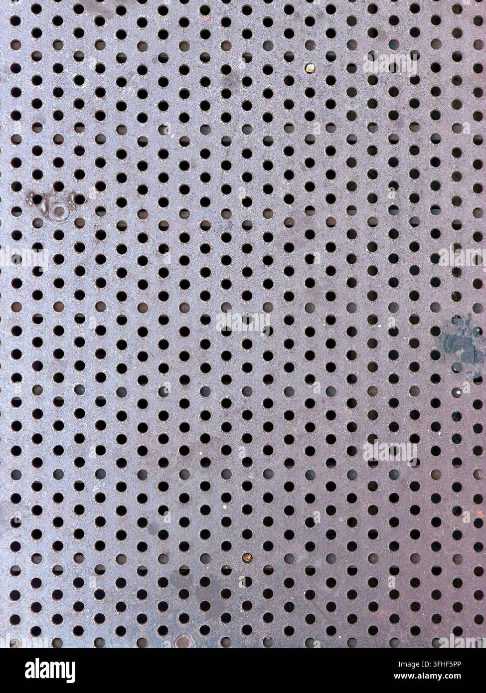Nahaufnahme einer gealterten perforierten Metalloberfläche mit einem gleichmäßigen Raster kreisförmiger Löcher und subtilen Gebrauchsspuren Stockfoto