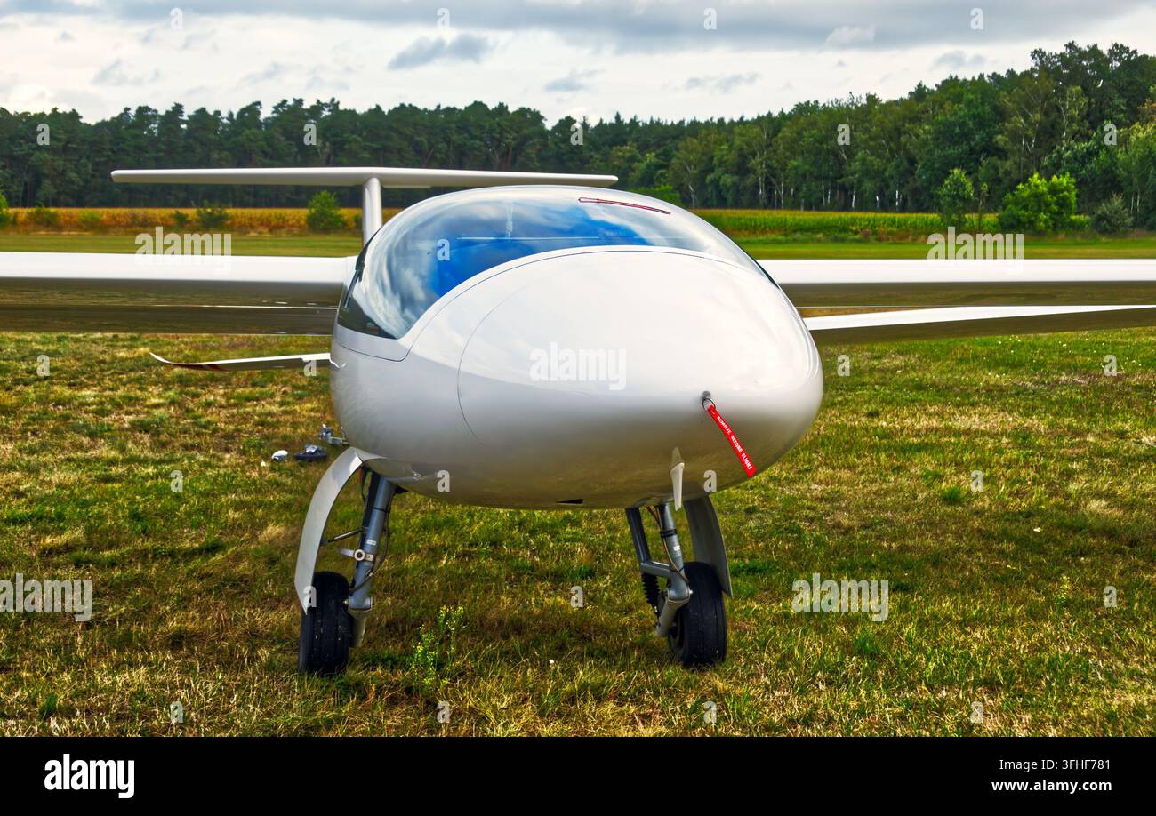 Weißes Gleitflugzeug steht auf einem grünen Grasflugplatz, mit einer sichtbar in der Hintergrund gegen einen bewölkten Himmel liegenden Landebahn Stockfoto