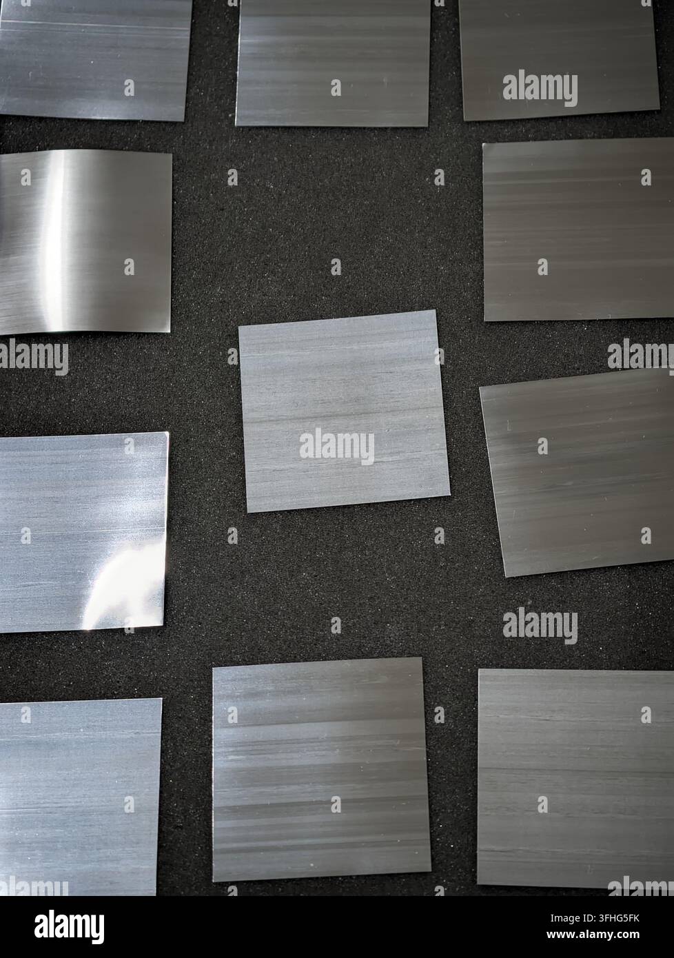 Mehrere gebürstete Metallproben in Silber- und Grautönen sind über dunklen, strukturierten Stoff angeordnet und erzeugen einen industriellen Texturkontrast, Material Stockfoto