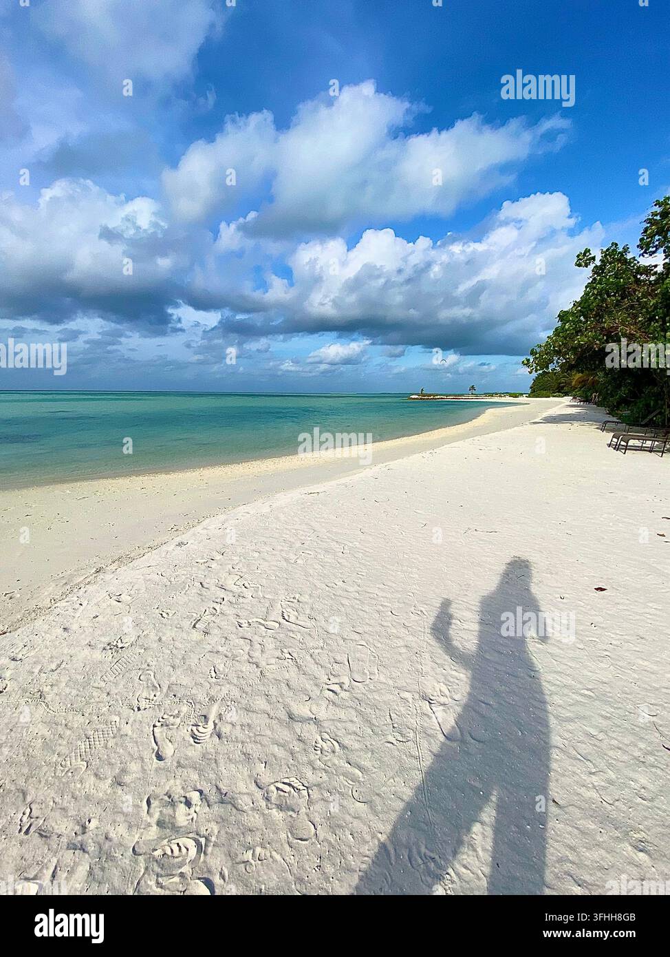 Breiter weißer Sandstrand neben türkisfarbener Lagune unter dramatischen tropischen Wolken. - Smartphone-aufgenommenes Stockfoto