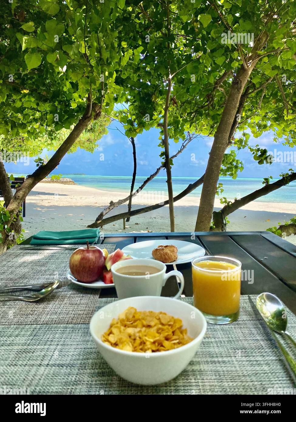Frühstück mit Müsli, Obst, Kaffee und Saft mit Blick auf einen tropischen Strand. - Smartphone-aufgenommenes Stockfoto