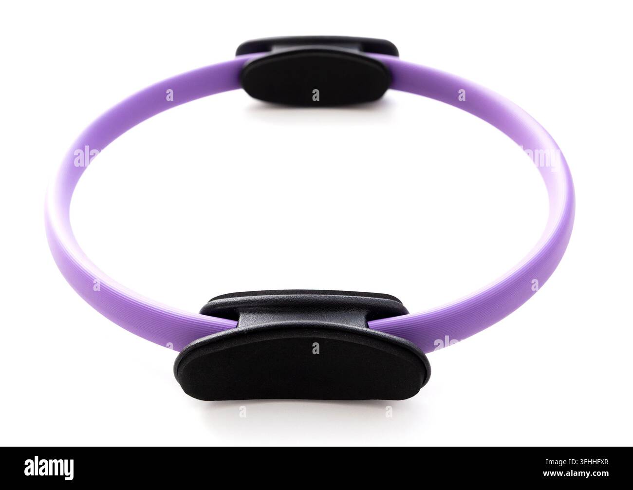 Ein violetter Pilates-Ring mit schwarzen Griffen liegt auf einem weißen Hintergrund Stockfoto