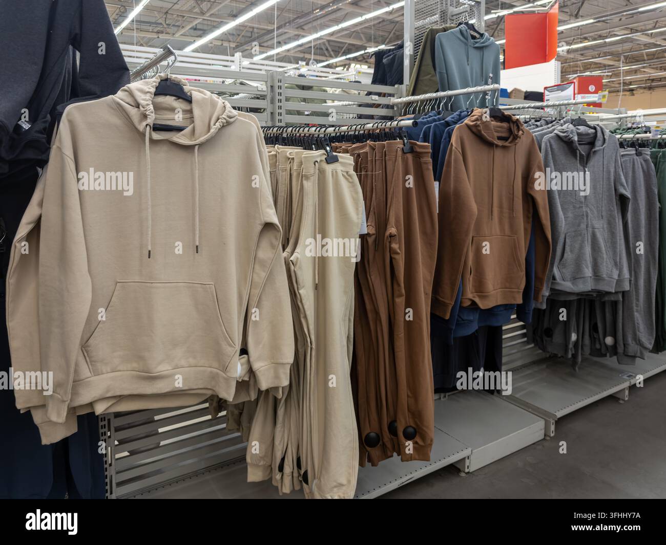 Verschiedene neutral gefärbte Sweatshirts und Jogginghosen, die auf Kleiderbügeln in einem Einzelhandelsgeschäft arrangiert sind, präsentieren die neuesten saisonalen Trends in erschwinglicher Streetwear Stockfoto
