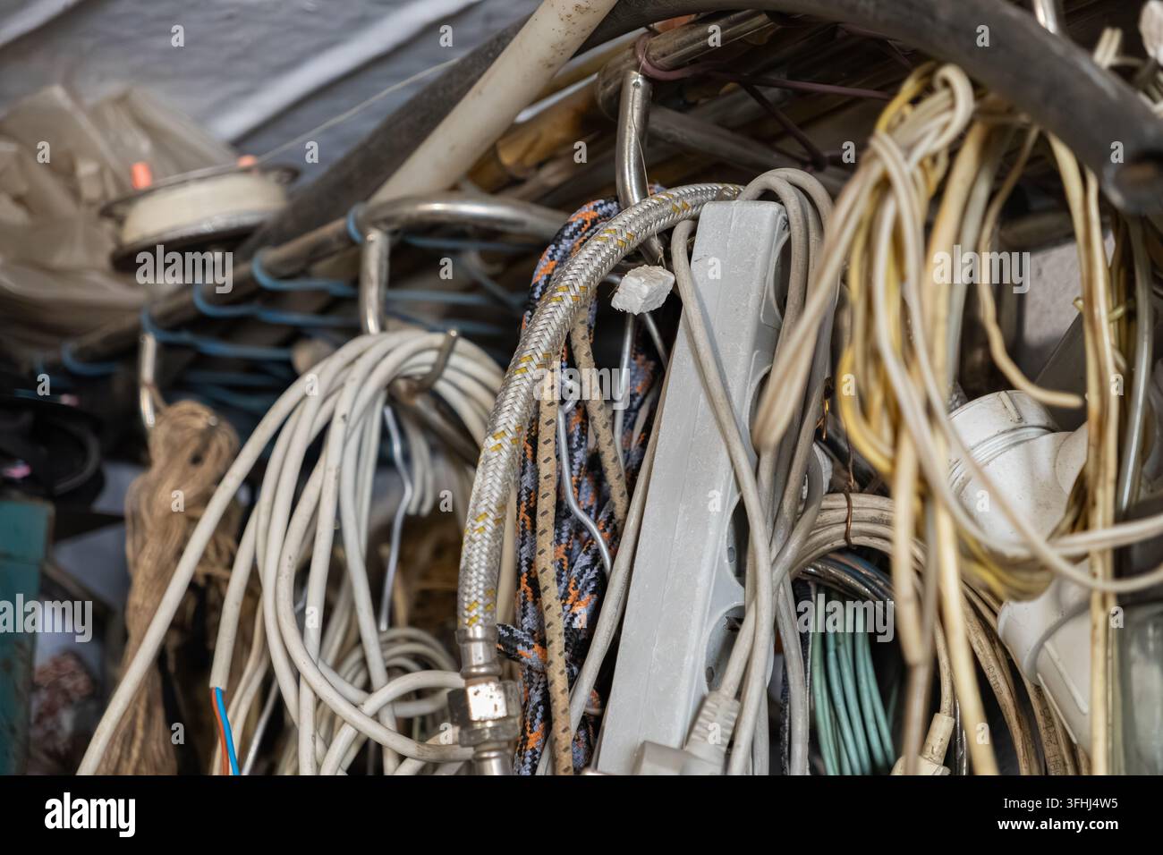 Unorganisierter Haufen von hängenden Kabeln, Steckdosenleisten und geflochtenen Schläuchen, die an Metallhaken gelagert sind und eine rohe visuelle Darstellung von industrieller Unordnung bieten Stockfoto