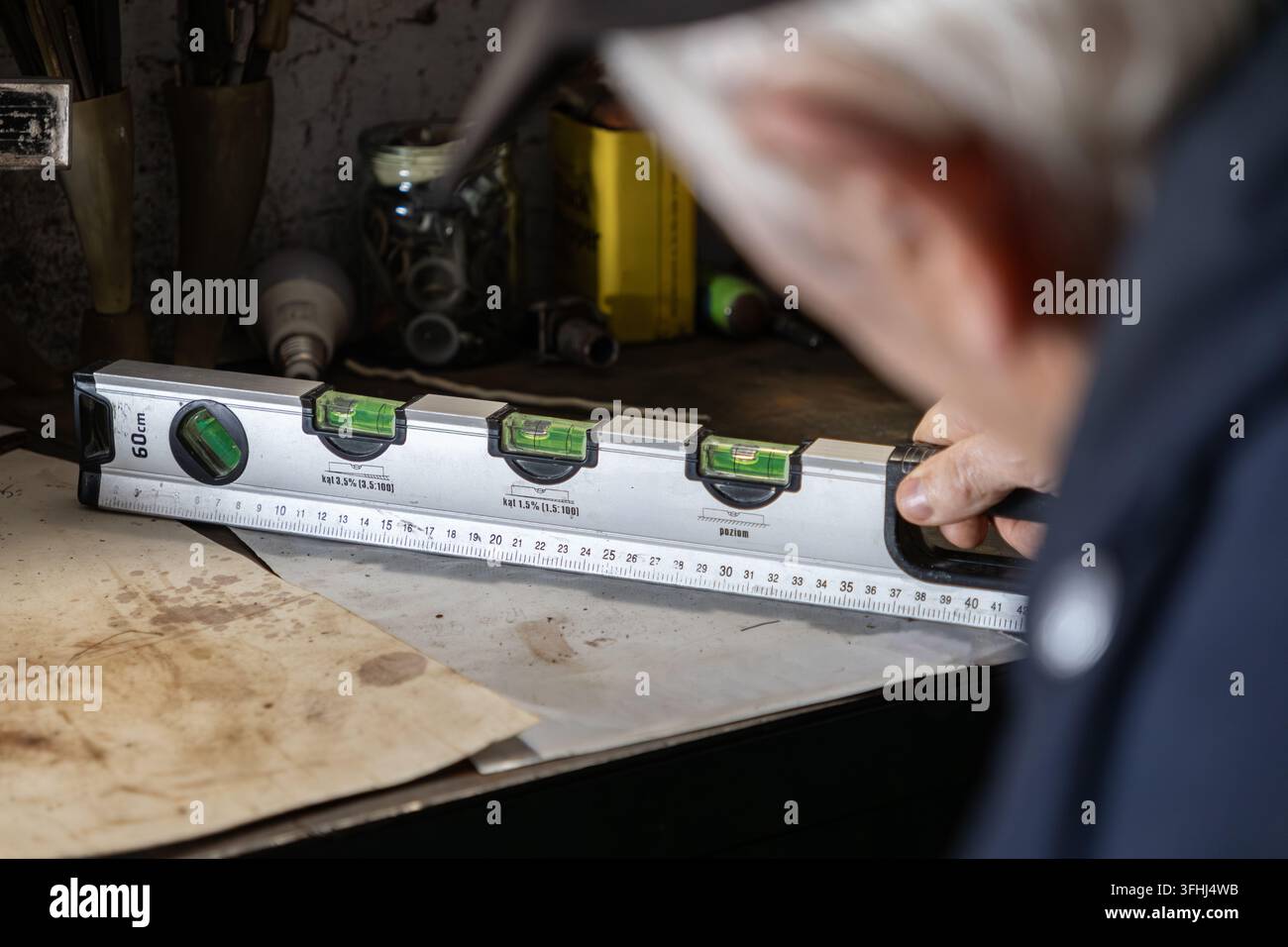 Ein erfahrener Zimmermann prüft die Ebenheit mit einem Metall-Libellenwerkzeug auf einer Holzoberfläche, was hochwertige Handwerkskunst und Sorgfalt betont Stockfoto