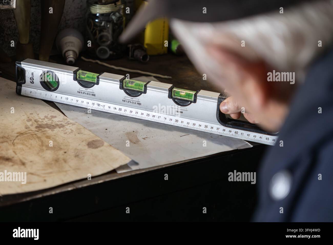 Ein konzentrierter Handwerker untersucht eine Metall-Wasserwaage auf einer Projektfläche und betont die Aufmerksamkeit für Details und genaue Messungen während eines traditionellen Stockfoto