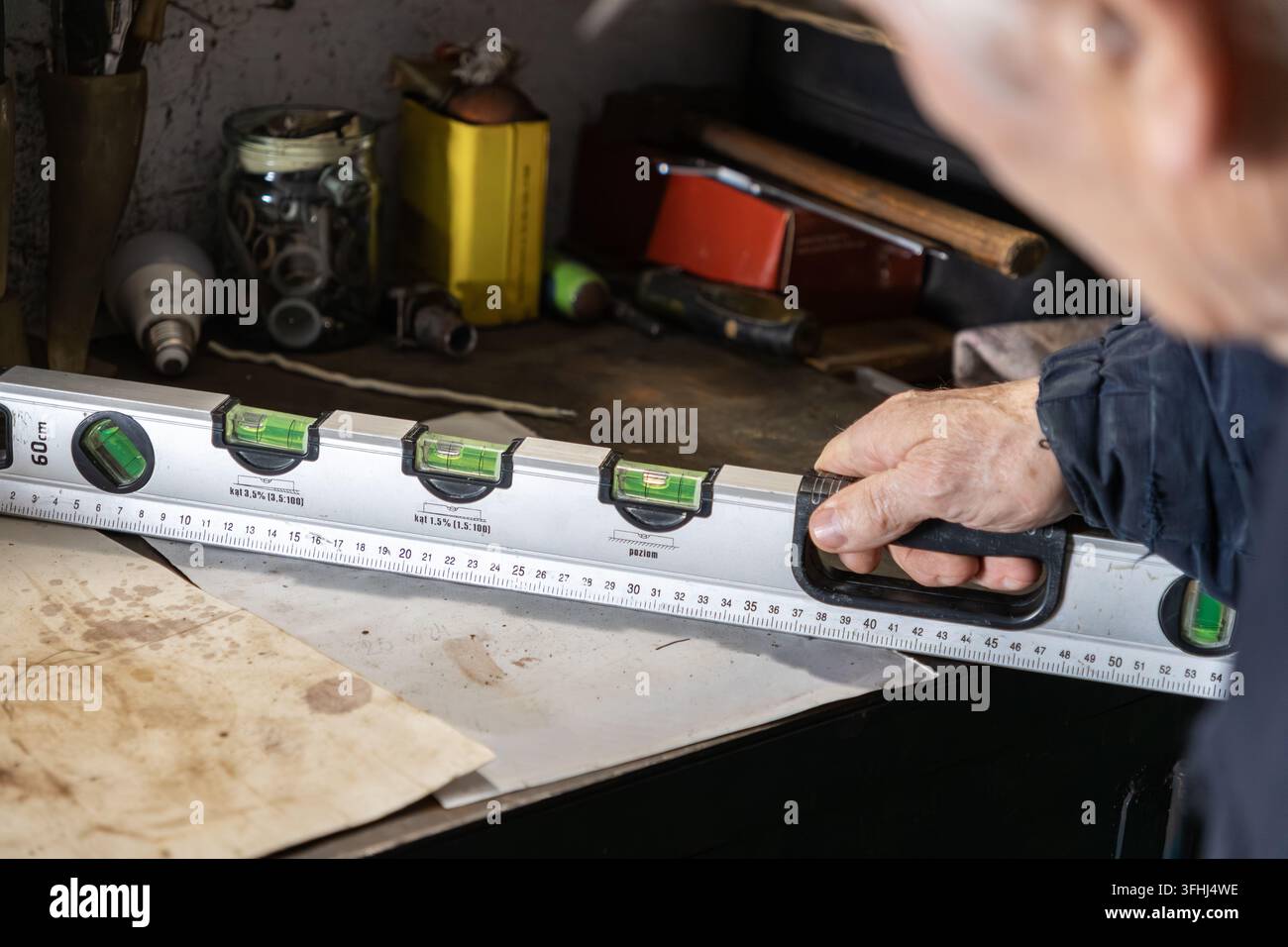 Ein erfahrener Bauarbeiter verwendet ein professionelles Werkzeug zur Messung der horizontalen Ausrichtung auf einem rustikalen Garagentisch, was den Handwerker betont Stockfoto
