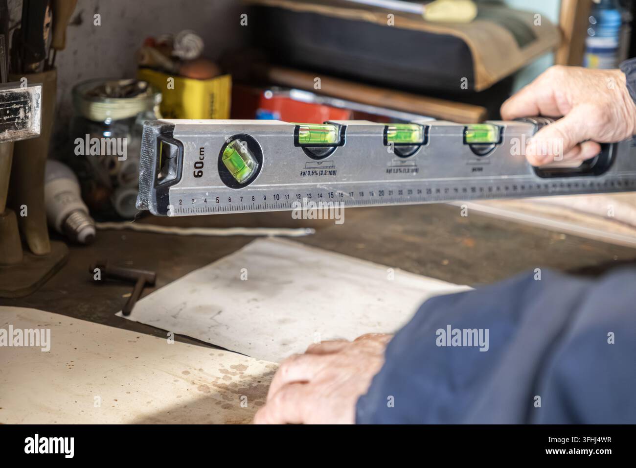 Ein erfahrener Handwerker verwendet eine Metall-Wasserwaage, um Genauigkeit zu gewährleisten, während er in einer rustikalen Werkstatt an einem Projekt arbeitet, was die Aufmerksamkeit für Details hervorhebt Stockfoto