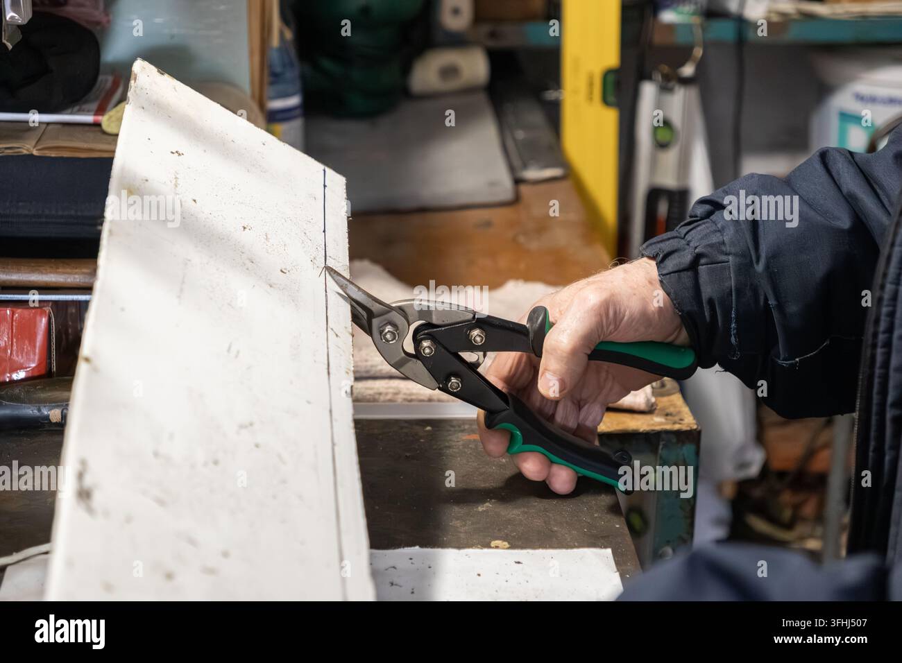 Hand hält Metallscheren und schneidet ein weißes Blatt an einem unordentlichen Arbeitstisch ab, betont detaillierte Renovierungsarbeiten und engagierte Handwerkskunst in einem traditionellen Stockfoto