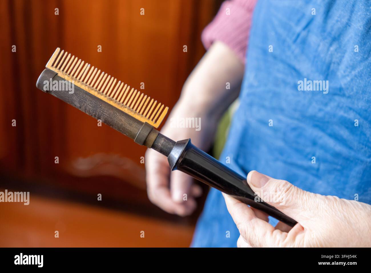 Der professionelle Friseur greift nach einem klassischen metallischen Glättekamm, der zum Glätten von Strähnen verwendet wird, und fängt das Erbe der Schönheitskunst und des Skis ein Stockfoto