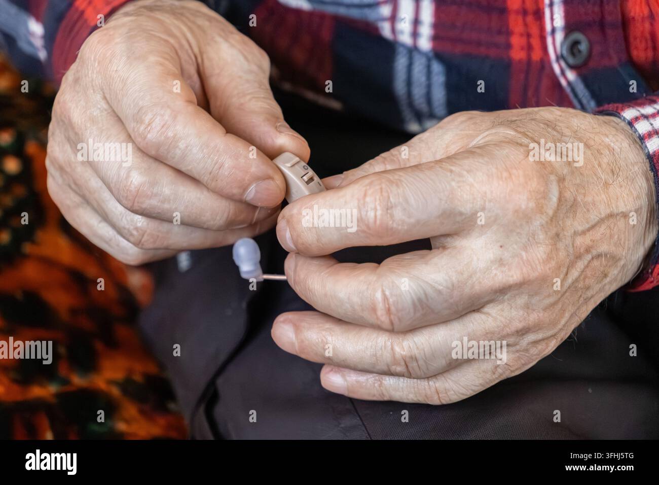 Senioren Hände handhaben sorgfältig ein beiges medizinisches Hörgerät, um Gesundheitsversorgung und alltägliche Hilfsmittel zu veranschaulichen, die die Kommunikation stärken Stockfoto