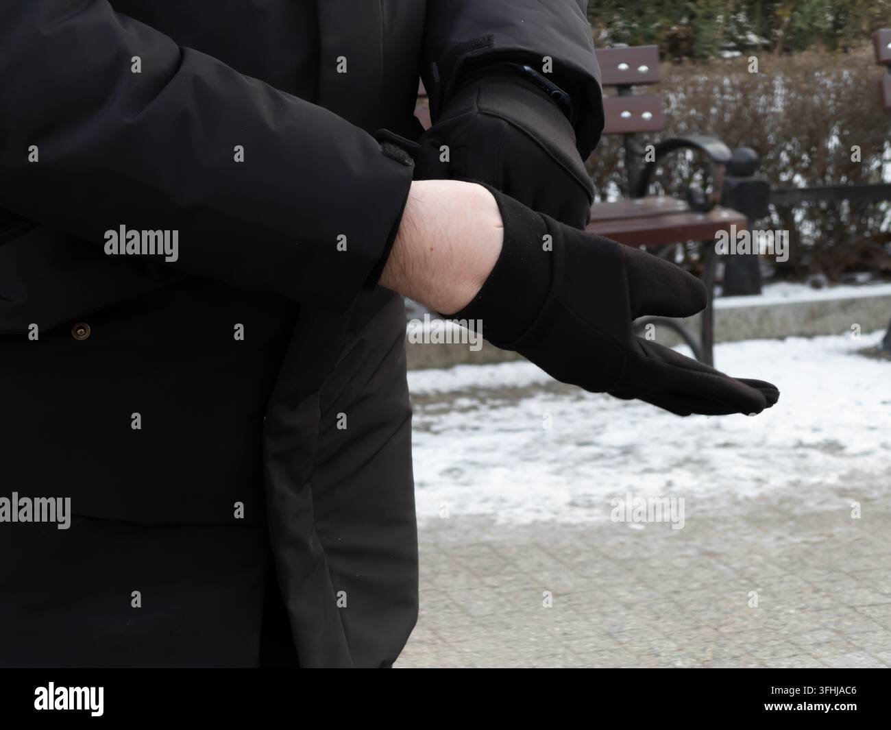 Eine Person zieht sich Thermohandschuhe während eines kalten Wintertages im Park an, um den praktischen Schutz gegen eisige Temperaturen mit wesentlichen g anzuzeigen Stockfoto