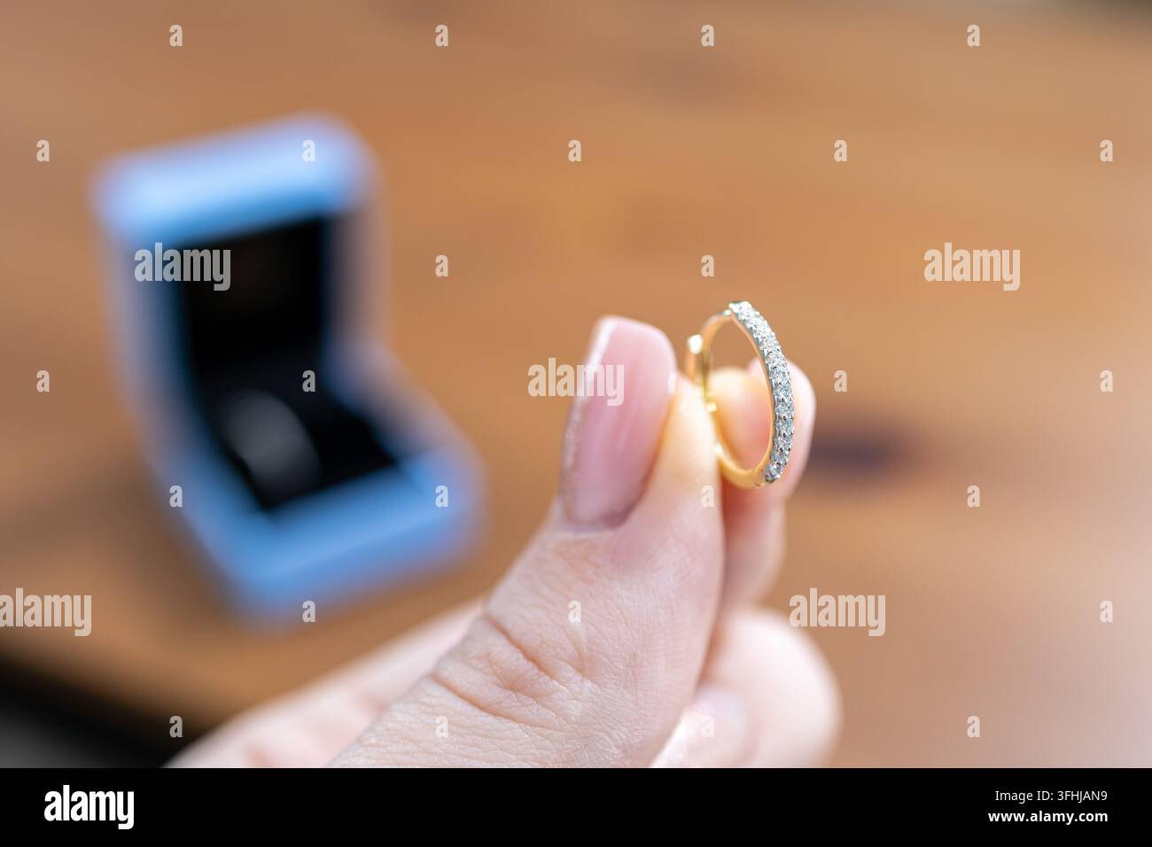 Elegante Hand, die einen verfeinerten goldenen Kreolenohrring hält, verziert mit winzigen Steinen, und feine Schmuckdetails und Premiumqualität für Geschenkideen in einem Stockfoto